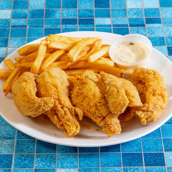 A white plate of golden fried fish fillets, french fries, and a side of tartar sauce on a blue tiled surface.