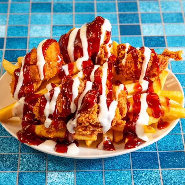 A plate of 4 Brothers Chicken & Fish fried chicken and fries drizzled with white sauce and barbecue sauce.