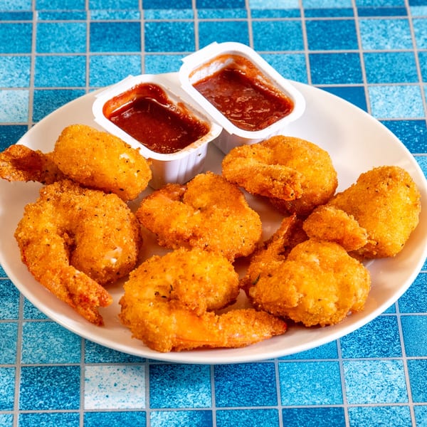 A plate of golden-brown fried shrimp with two containers of dipping sauce on a blue tiled surface.