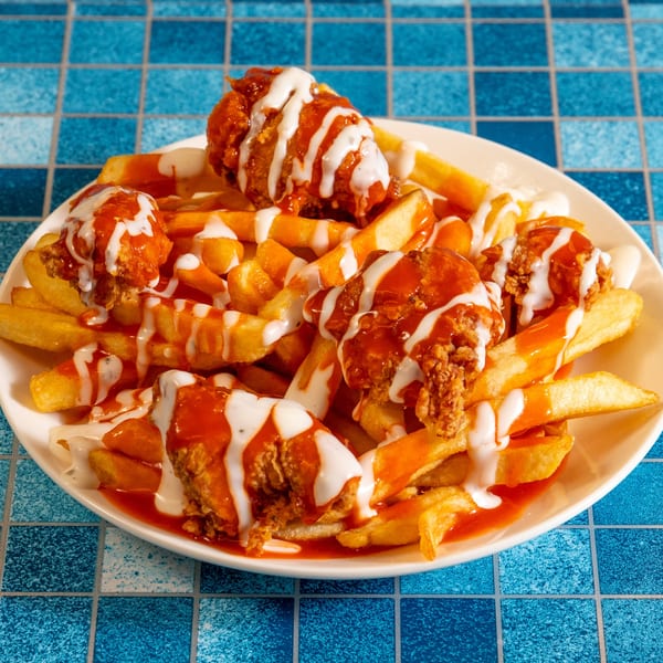 A plate of 4 Brothers Chicken & Fish fried chicken and fries, drizzled with buffalo and ranch sauce.