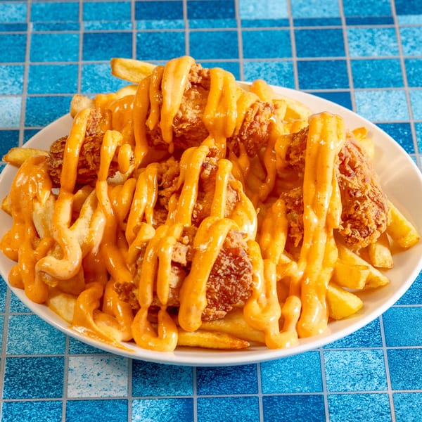 A white plate of 4 Brothers Chicken & Fish fried chicken and fries, drizzled with cheese sauce.