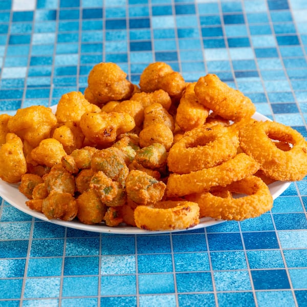 A white plate piled high with golden-brown fried okra, onion rings, and hushpuppies on a blue tiled surface.